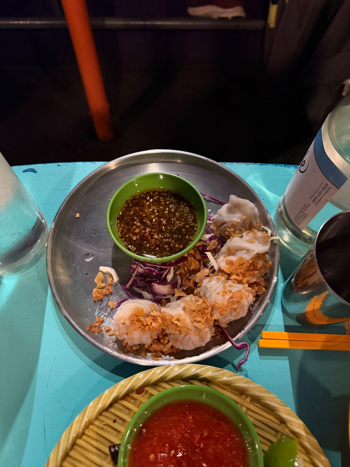 Dumplings Shumai de Cang Tin en una bandeja de metal, con una salsa oscura y trocitos crocantes por encima