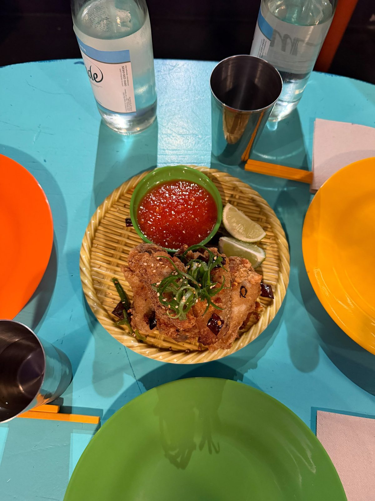 Mala Chicken Wings de Cang Tin sobre una bandeja de mimbre, con salsa roja y lima, en una mesa turquesa
