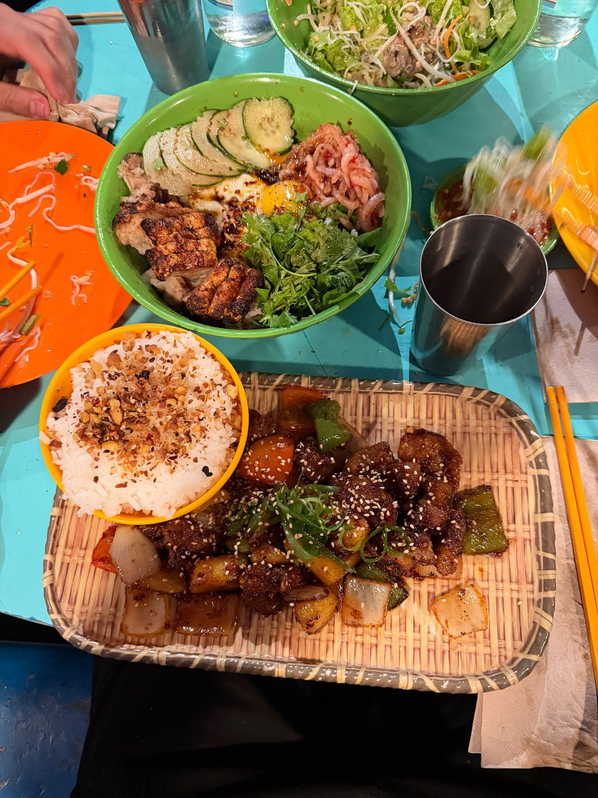 Mesa turquesa de Cang Tin, en Palermo, con el crispy pork en un bol verde, el Pad Prew Wan Moo sobre una bandeja de mimbre, arroz y platos de colores