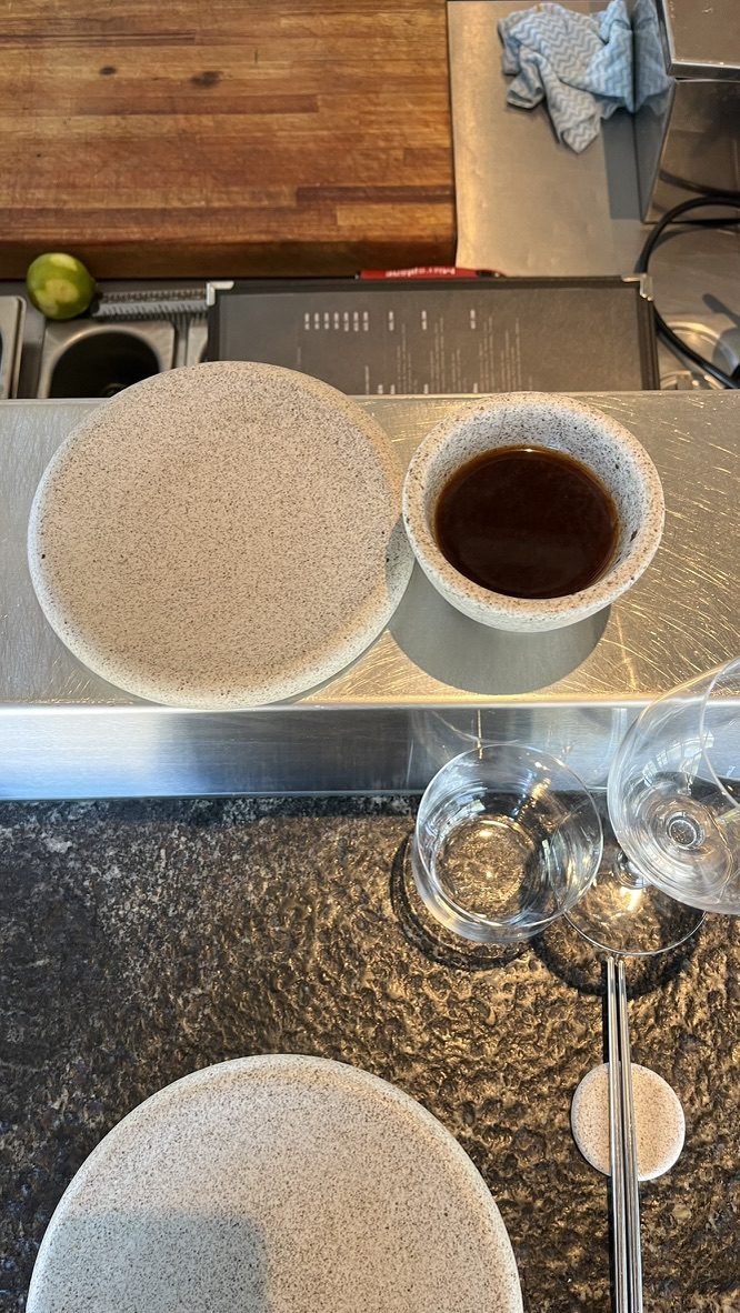Sopa miso en un bol de cerámica moteada sobre la barra de acero de Crudo Barra, junto a los platos de piedra, los vasos y los palitos