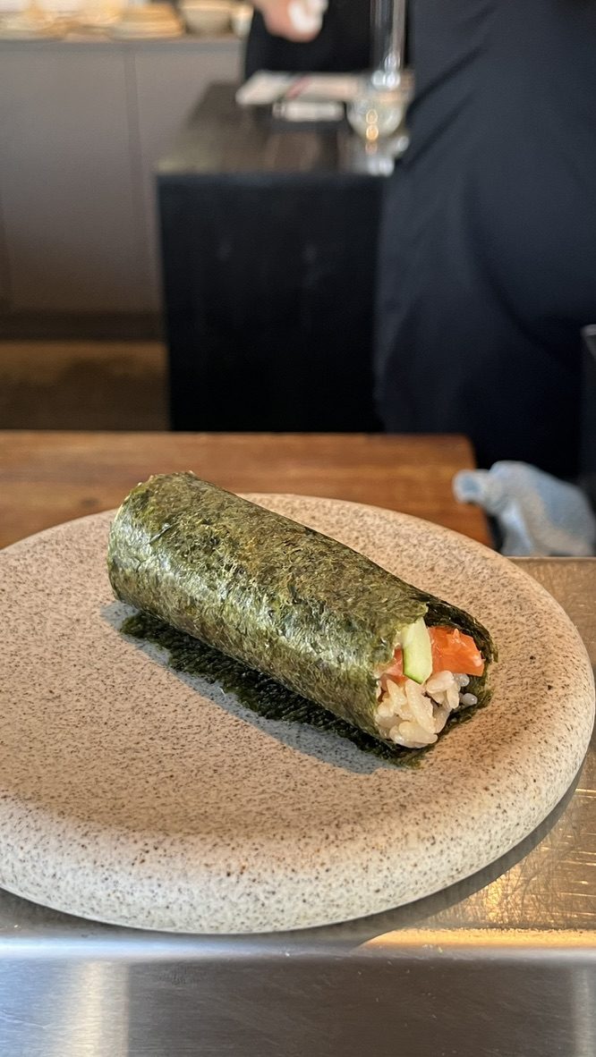 Handroll de trucha con alioli de chile y pepino fresco sobre un plato de piedra en la barra de Crudo Barra