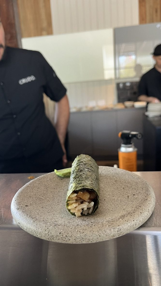 Handroll de trucha con aceite de trufa y polvo umami parado sobre un plato de piedra, con wasabi, en la barra de Crudo Barra