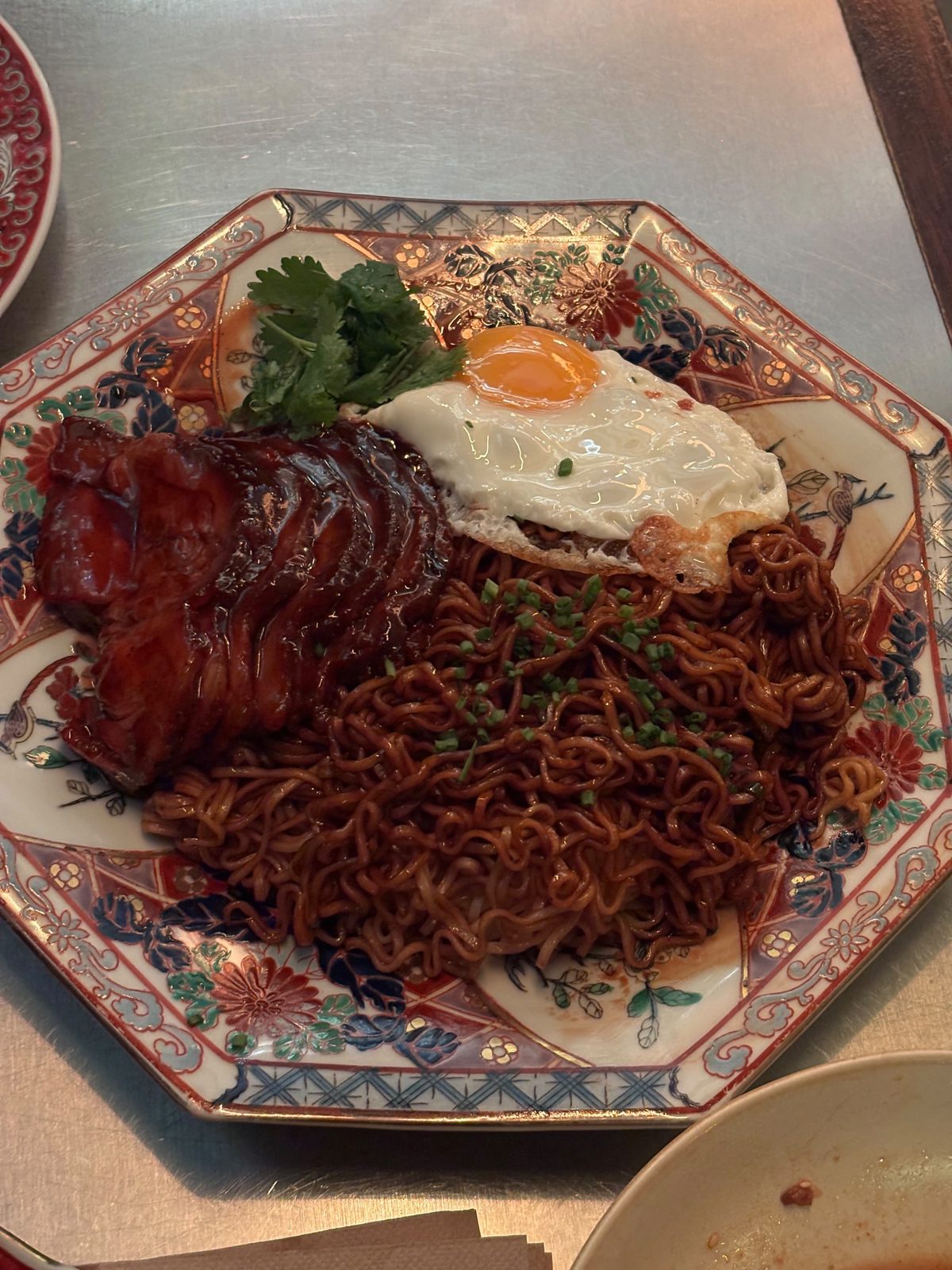 Char Siu Noodles de Tony Wu: fideos salteados con cerdo laqueado, un huevo frito y cilantro en un plato octogonal de porcelana pintada