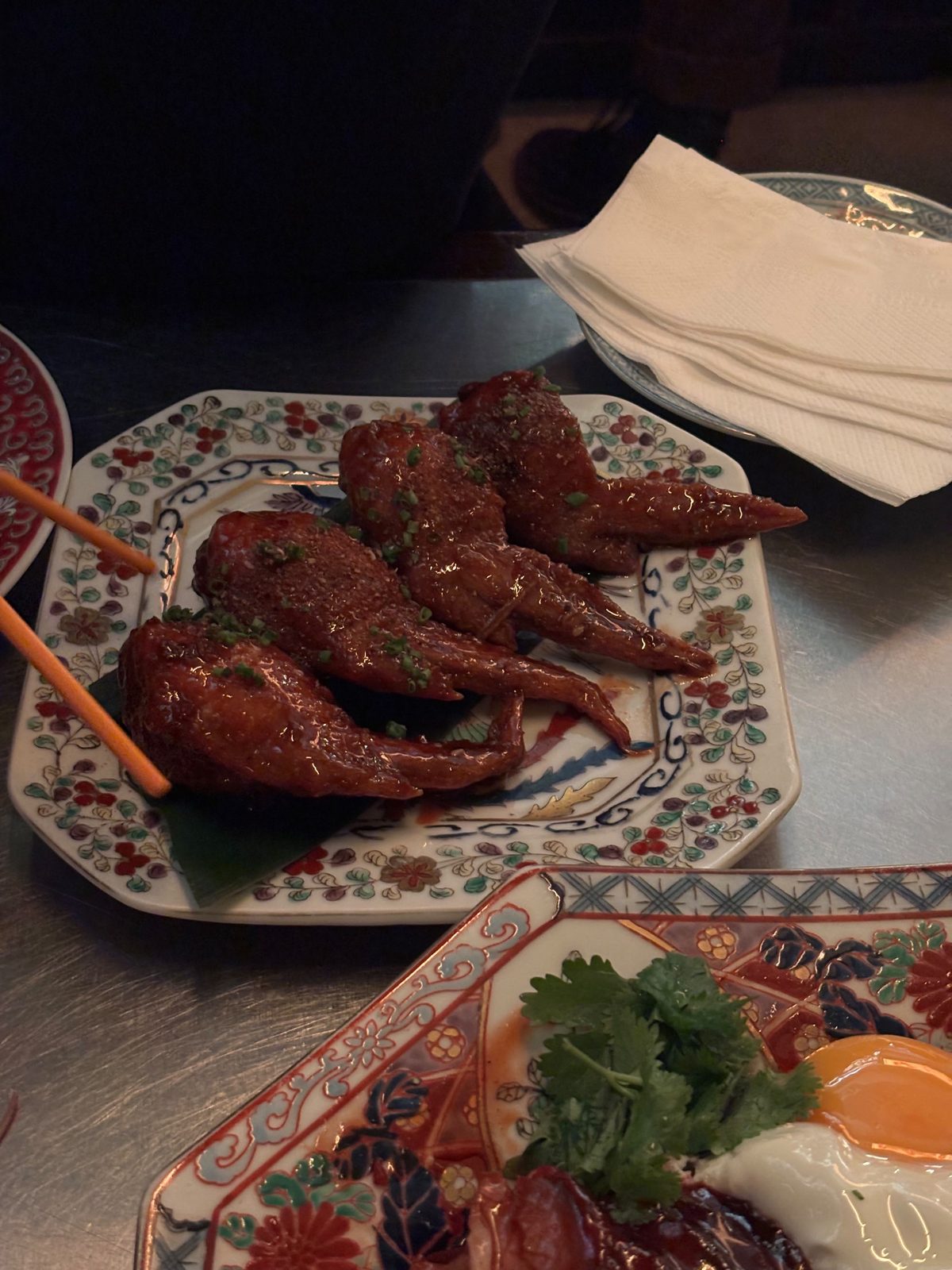 Stuffed Chicken Wings de Tony Wu: cuatro alitas laqueadas rellenas sobre una hoja verde, en un plato de porcelana con flores pintadas